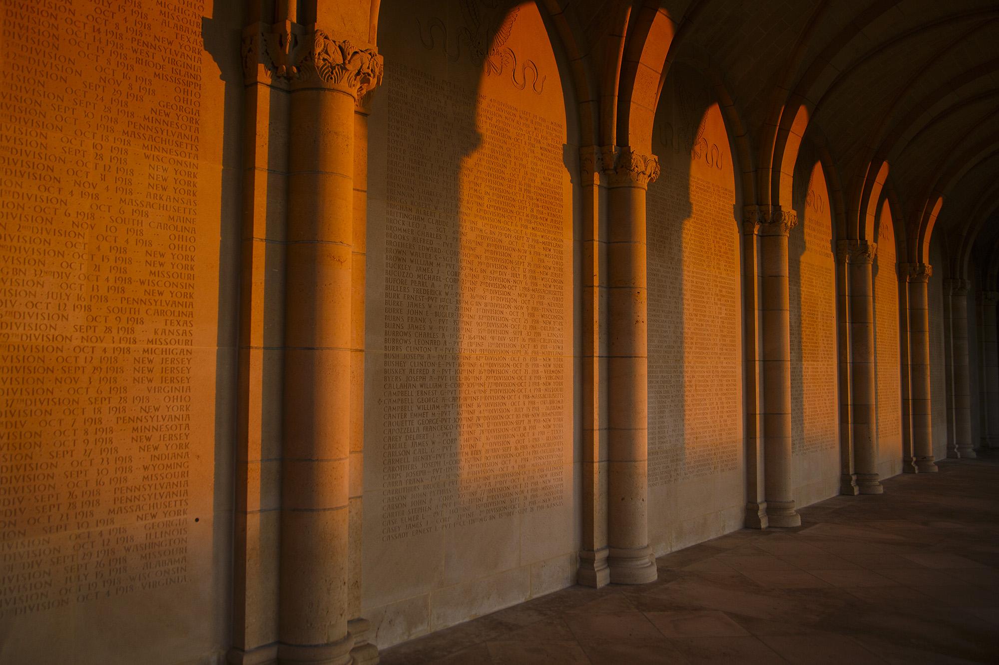 Color photograph of stone walls engraved with names, bathed in sunset light.